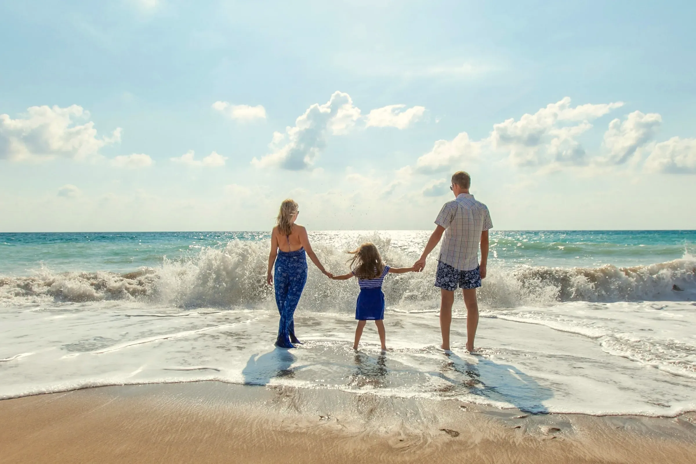 Familj som håller varandra i händerna i vattenbrynet och blickar ut över havet